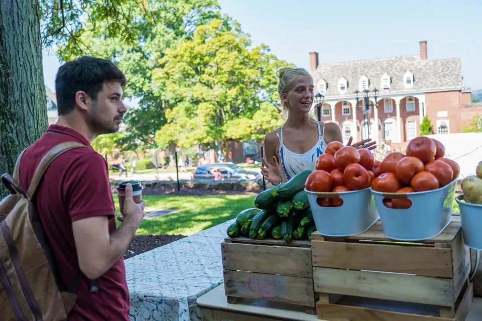 A student speaking with a produce vendor at the WVU Farmer's market